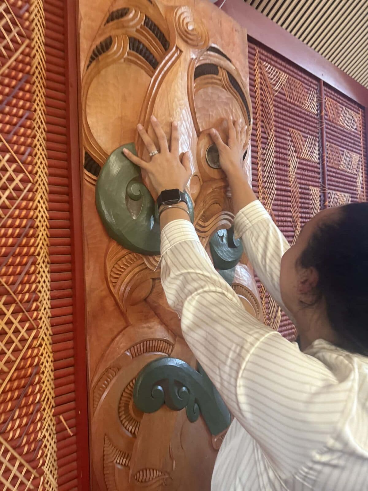Hands touching whakairo carvings in the wharenui